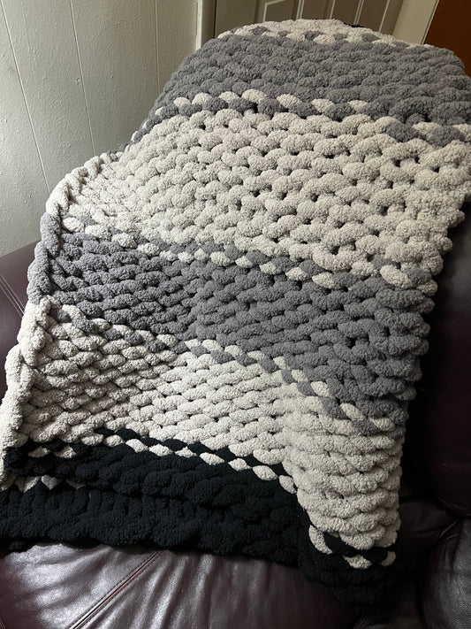 Dark gray, Light Gray, and black hand crocheted blanket laying over a brown couch