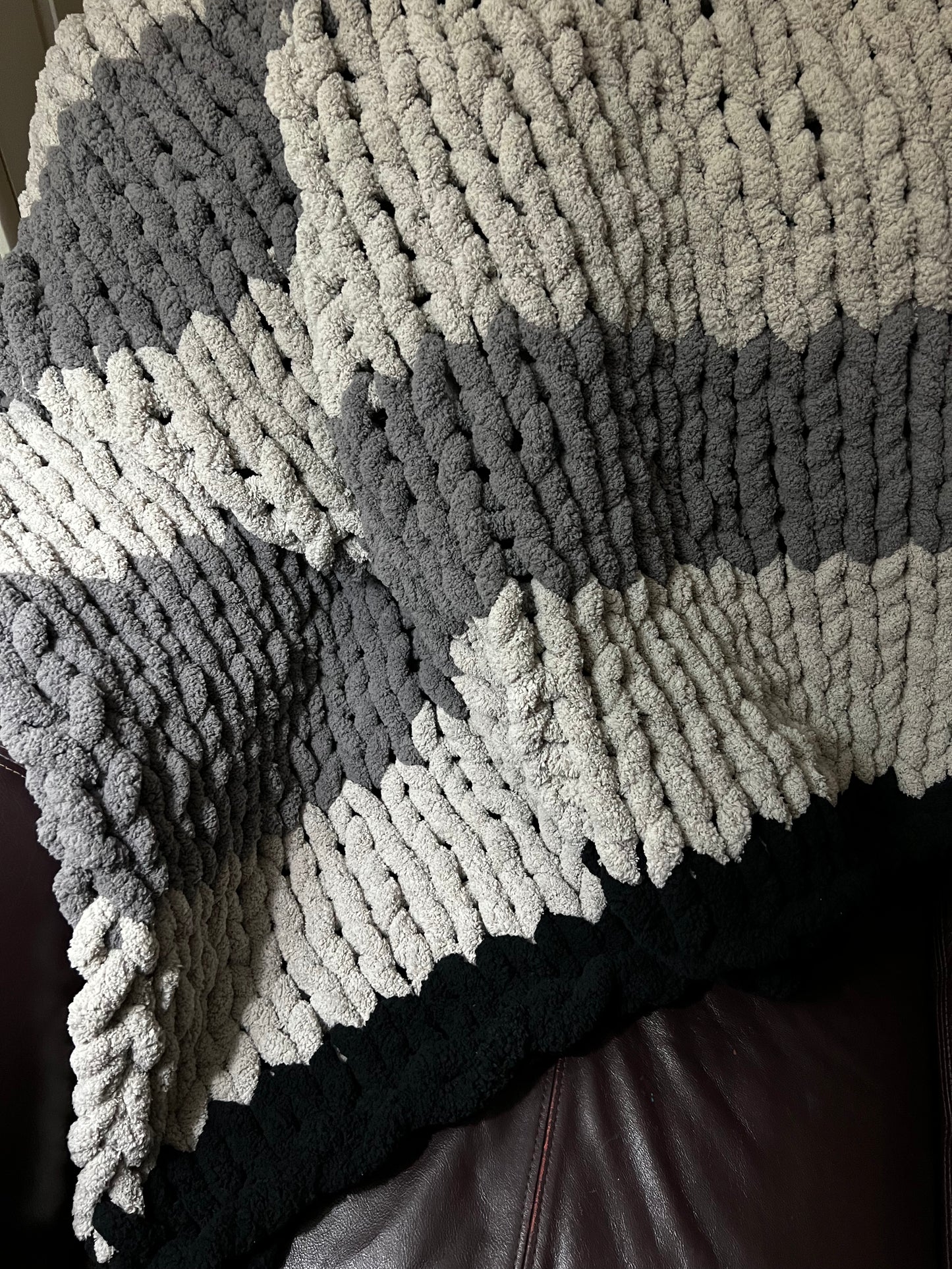 Dark gray, Light Gray, and black hand crocheted blanket laying over a brown couch