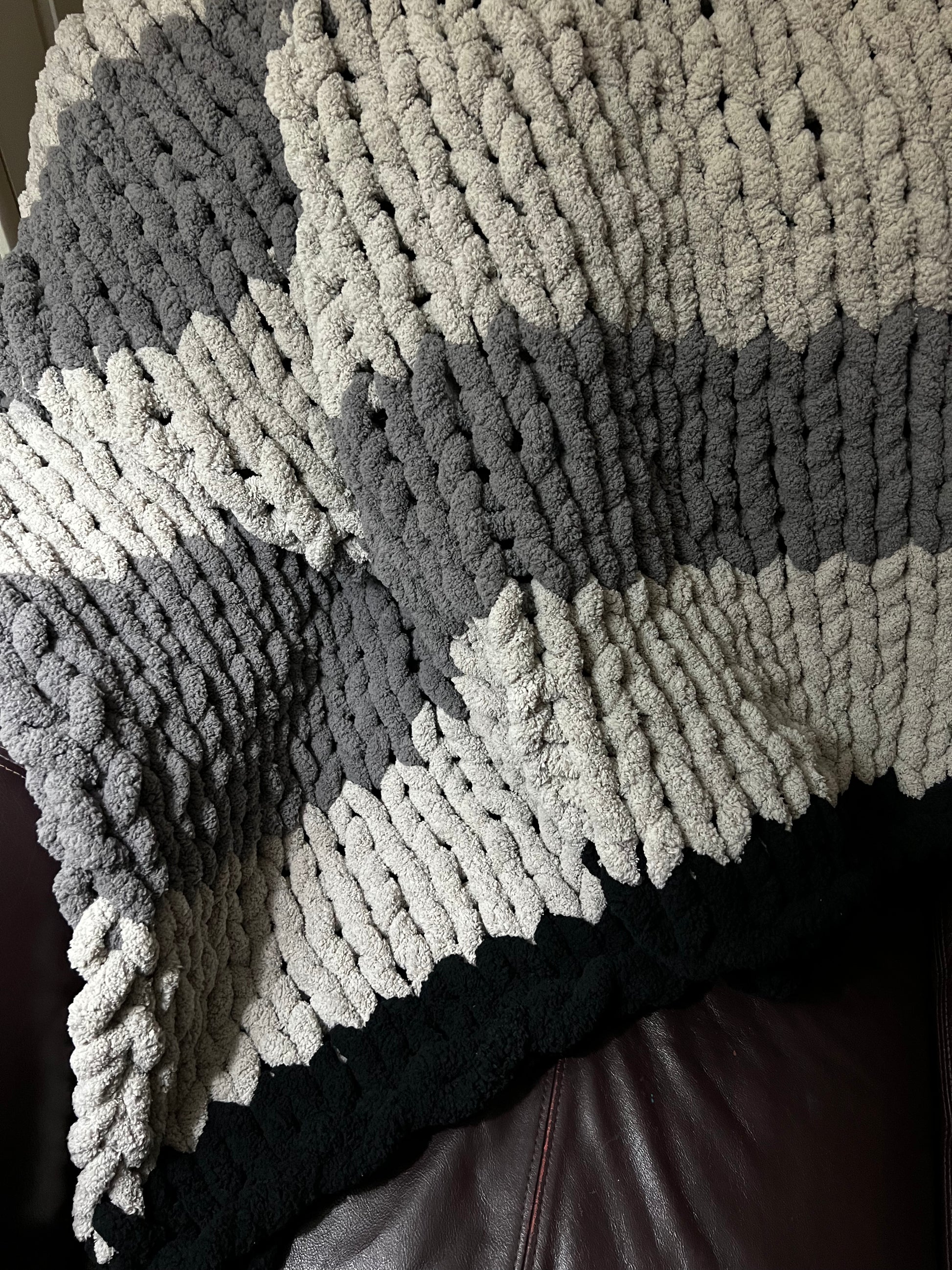 Dark gray, Light Gray, and black hand crocheted blanket laying over a brown couch