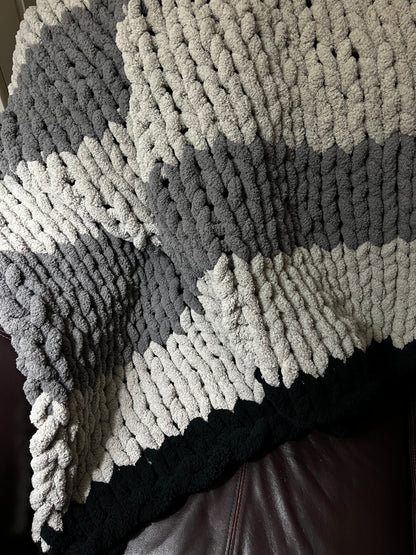 Dark gray, Light Gray, and black hand crocheted blanket laying over a brown couch