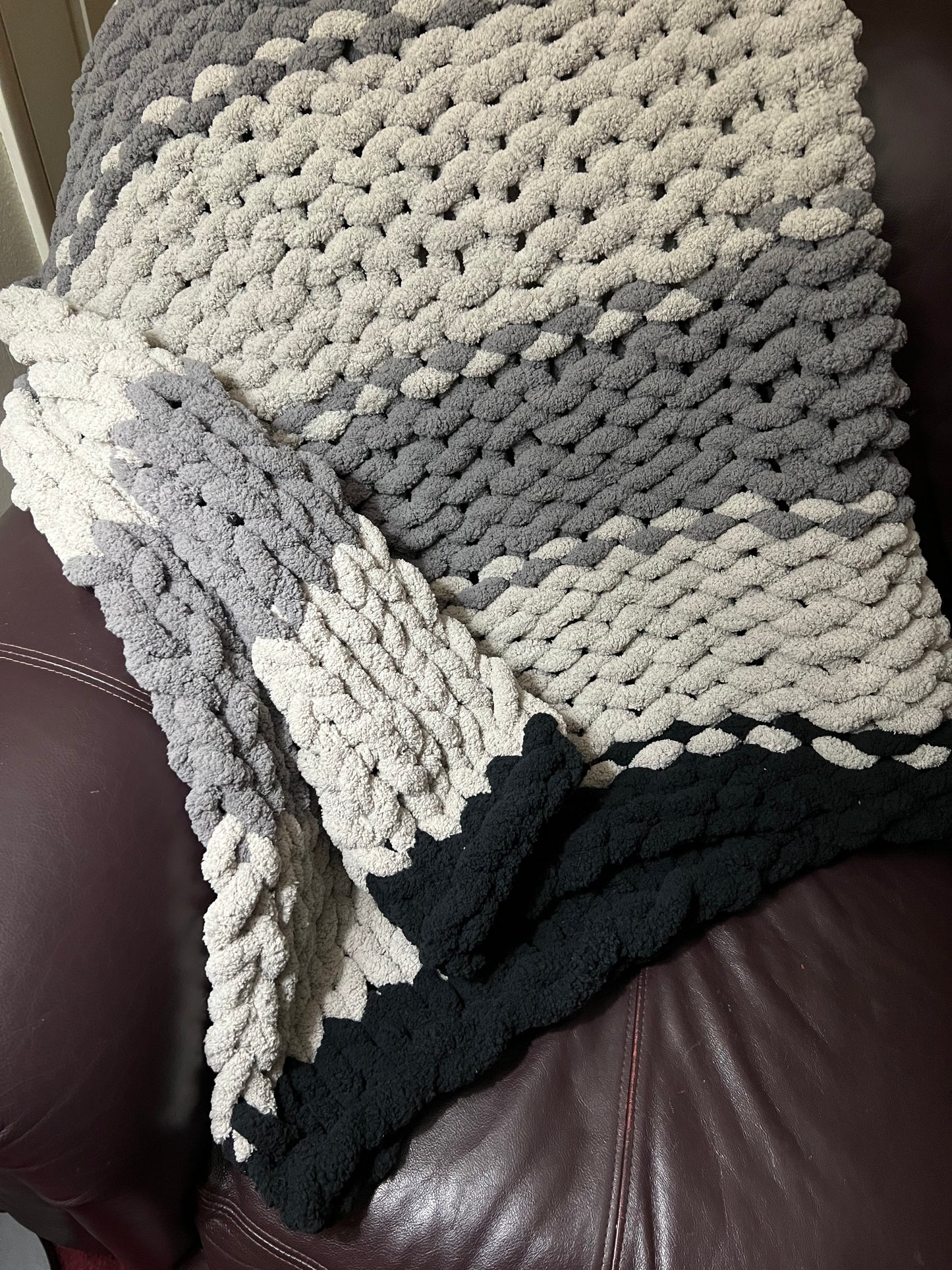Dark gray, Light Gray, and black hand crocheted blanket laying over a brown couch