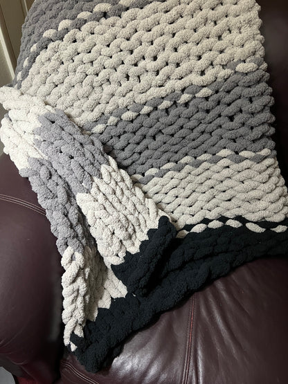 Dark gray, Light Gray, and black hand crocheted blanket laying over a brown couch