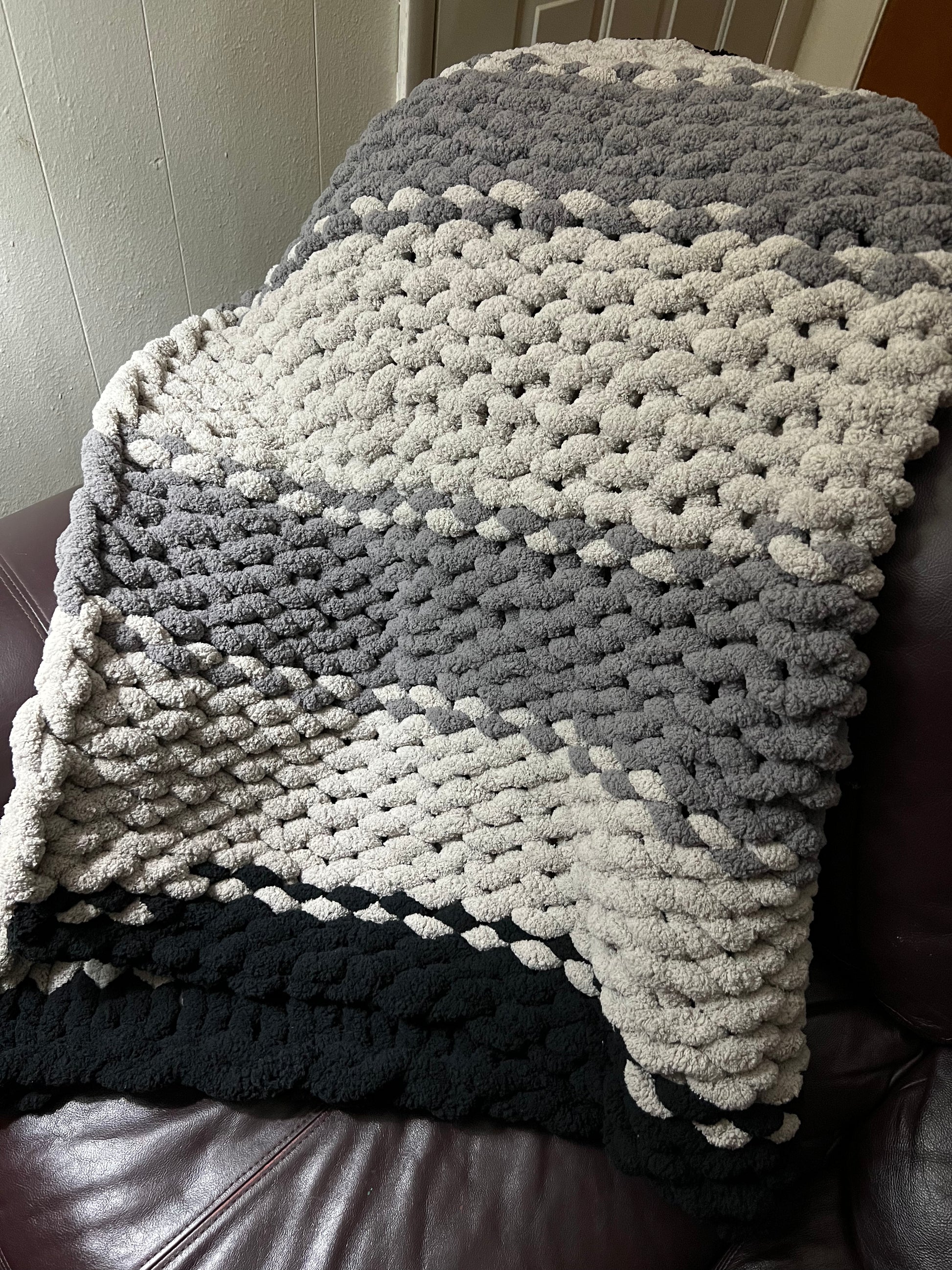 Dark gray, Light Gray, and black hand crocheted blanket laying over a brown couch
