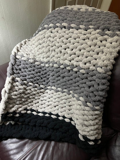 Dark gray, Light Gray, and black hand crocheted blanket laying over a brown couch